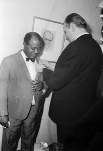 Unter dem Porträtbild von Ministerpräsident Otto Grotewohl bekommt der amerikanische Jazzmusiker Louis Armstrong in Ost Berlin eine Ehrennadel ans Revers gesteckt, DDR 1965.
(C) United Archives/Tassilo Leher